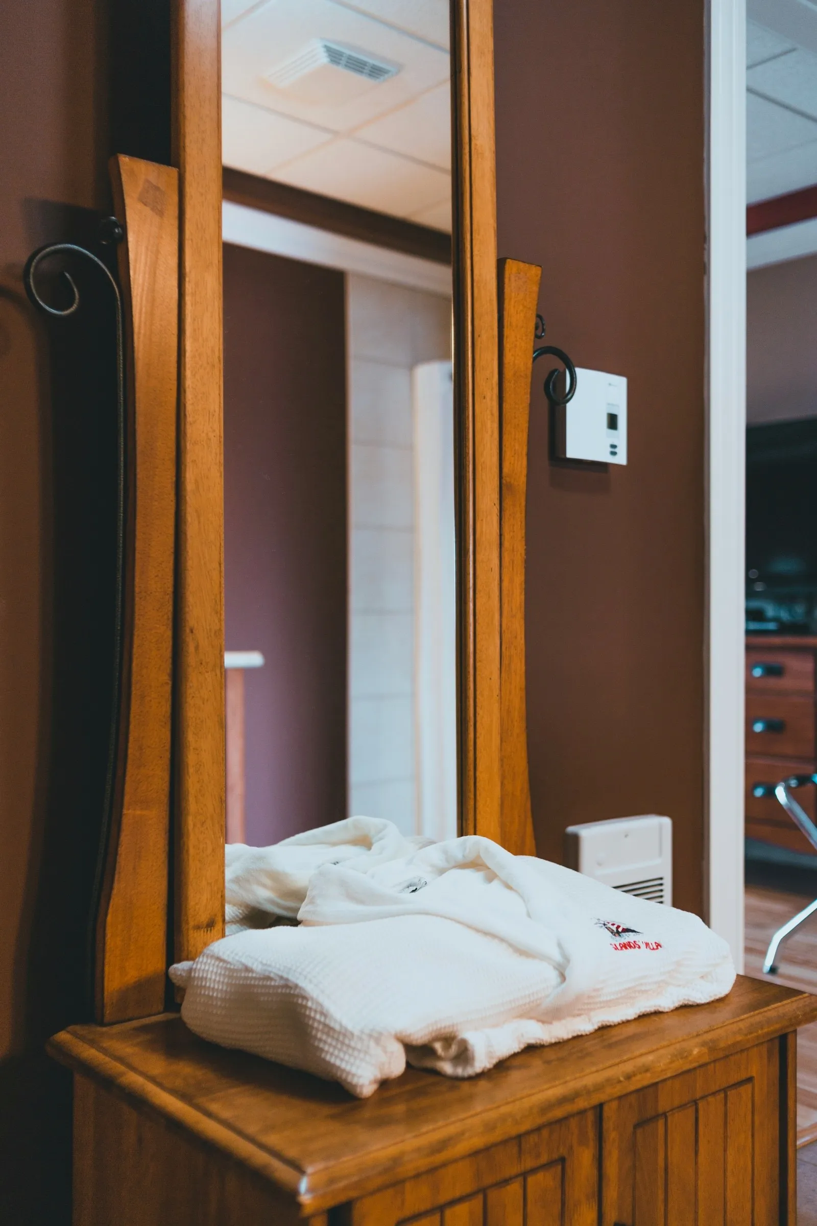 Folded waffle-weave bathrobes embroidered with the Islands' Villa name, stacked on a dresser beneath a mirror