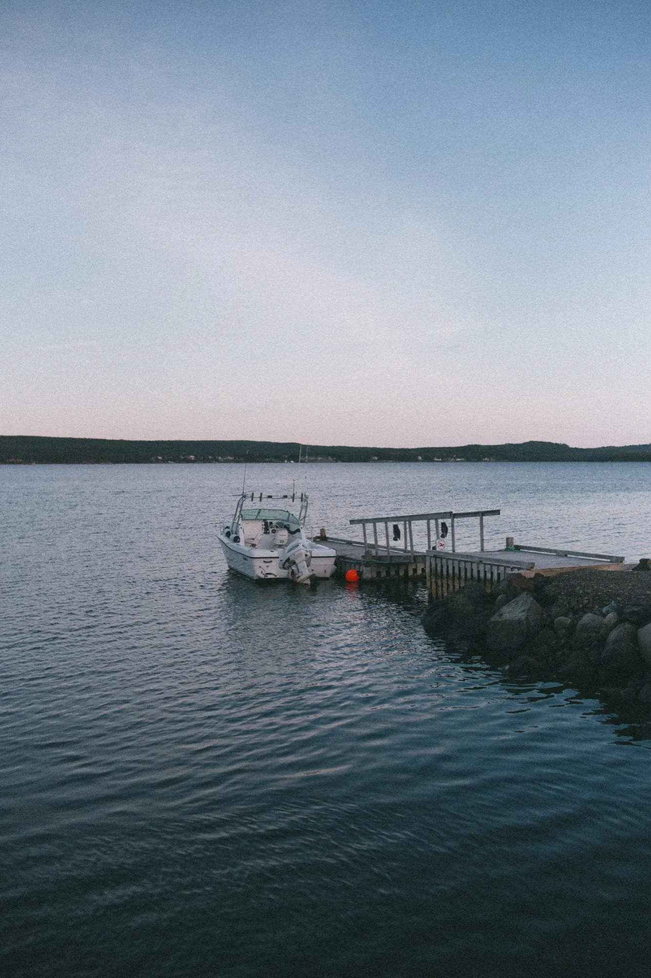 A boat lying still at the dock as the light goes down over the water