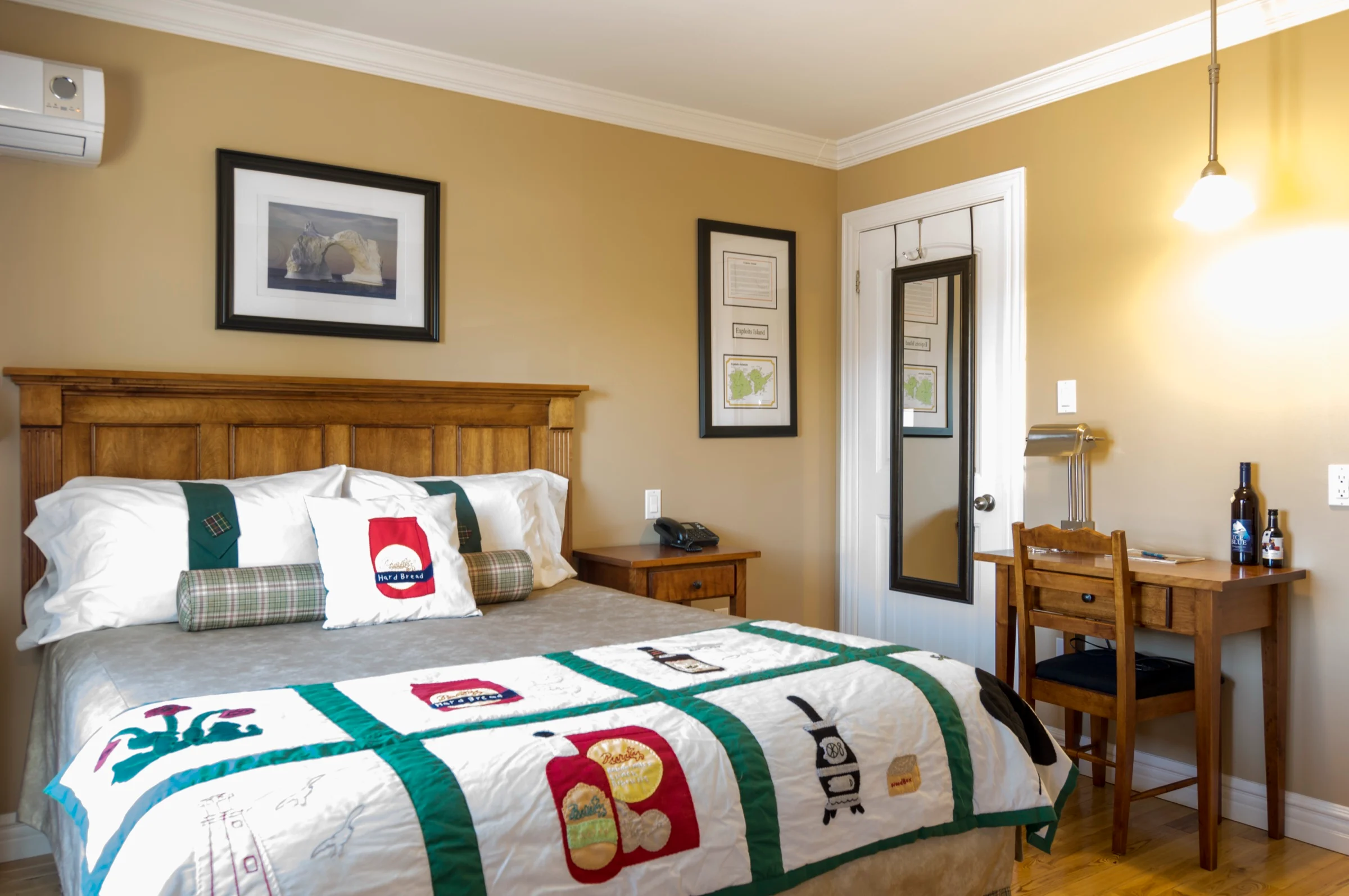Queen Room with a queen bed in a Newfoundland quilt, a writing desk and lamp beside it, and a framed iceberg photograph on the wall