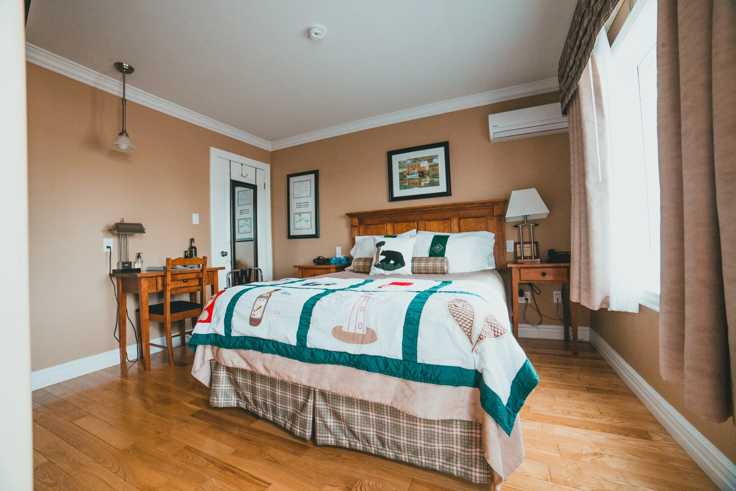 Wide view of the Queen Room showing the queen bed, the desk under the window and curtains drawn back to the daylight