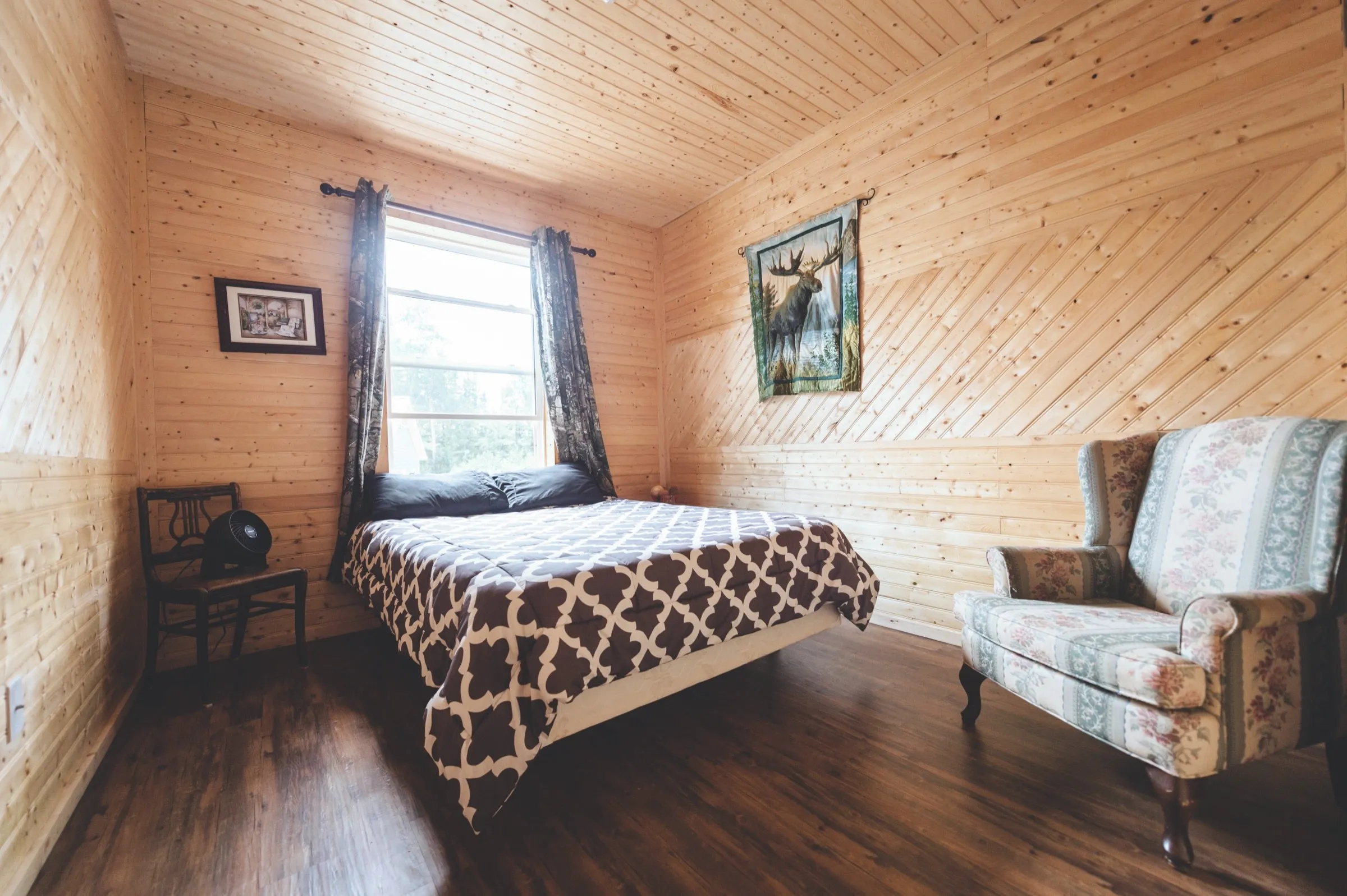 Chalet bedroom with a queen bed under a patterned comforter, a wingback armchair and a moose wall hanging