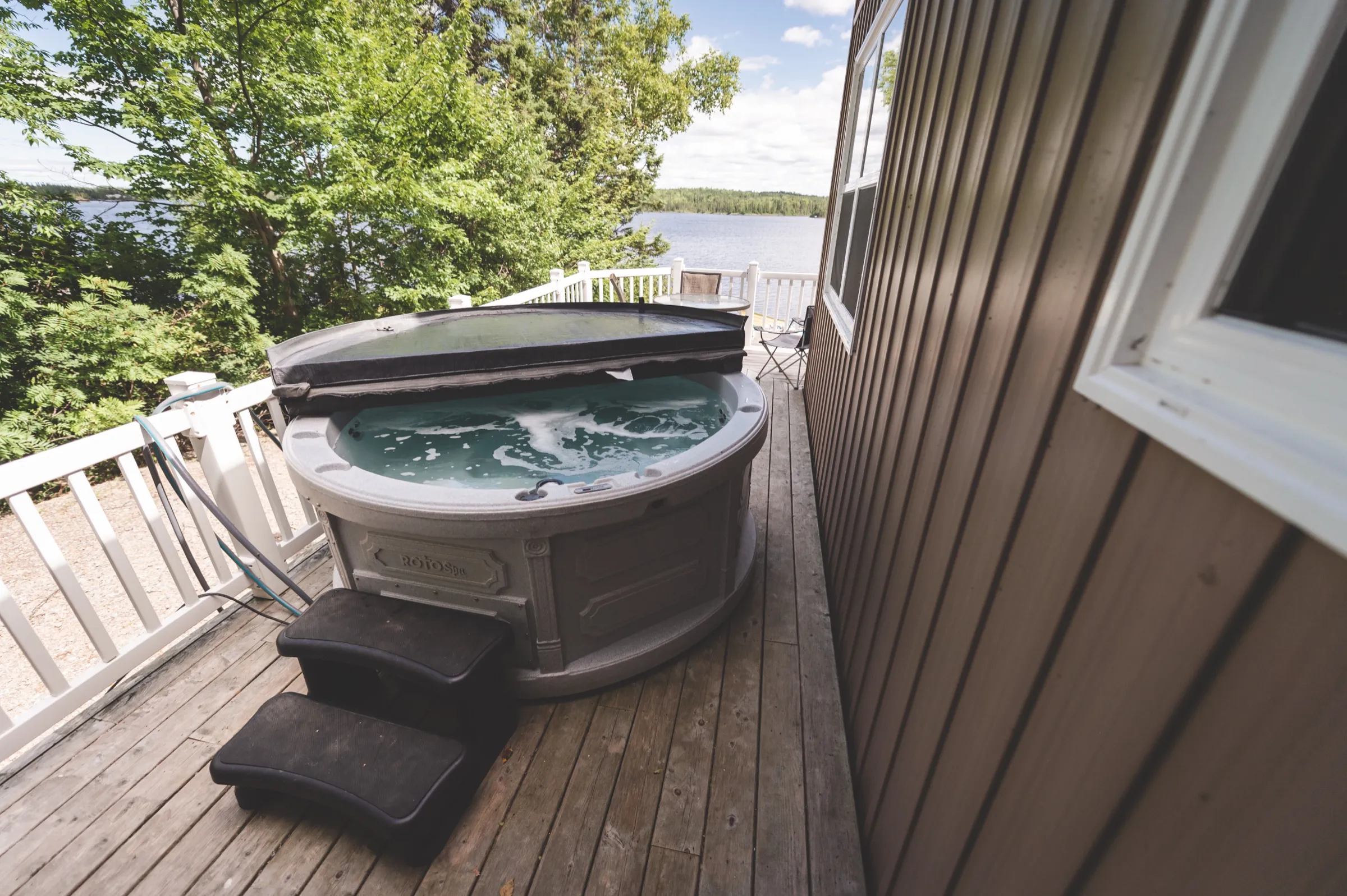 Hot tub on the chalet deck, sheltered by the building and looking out toward the trees and the pond