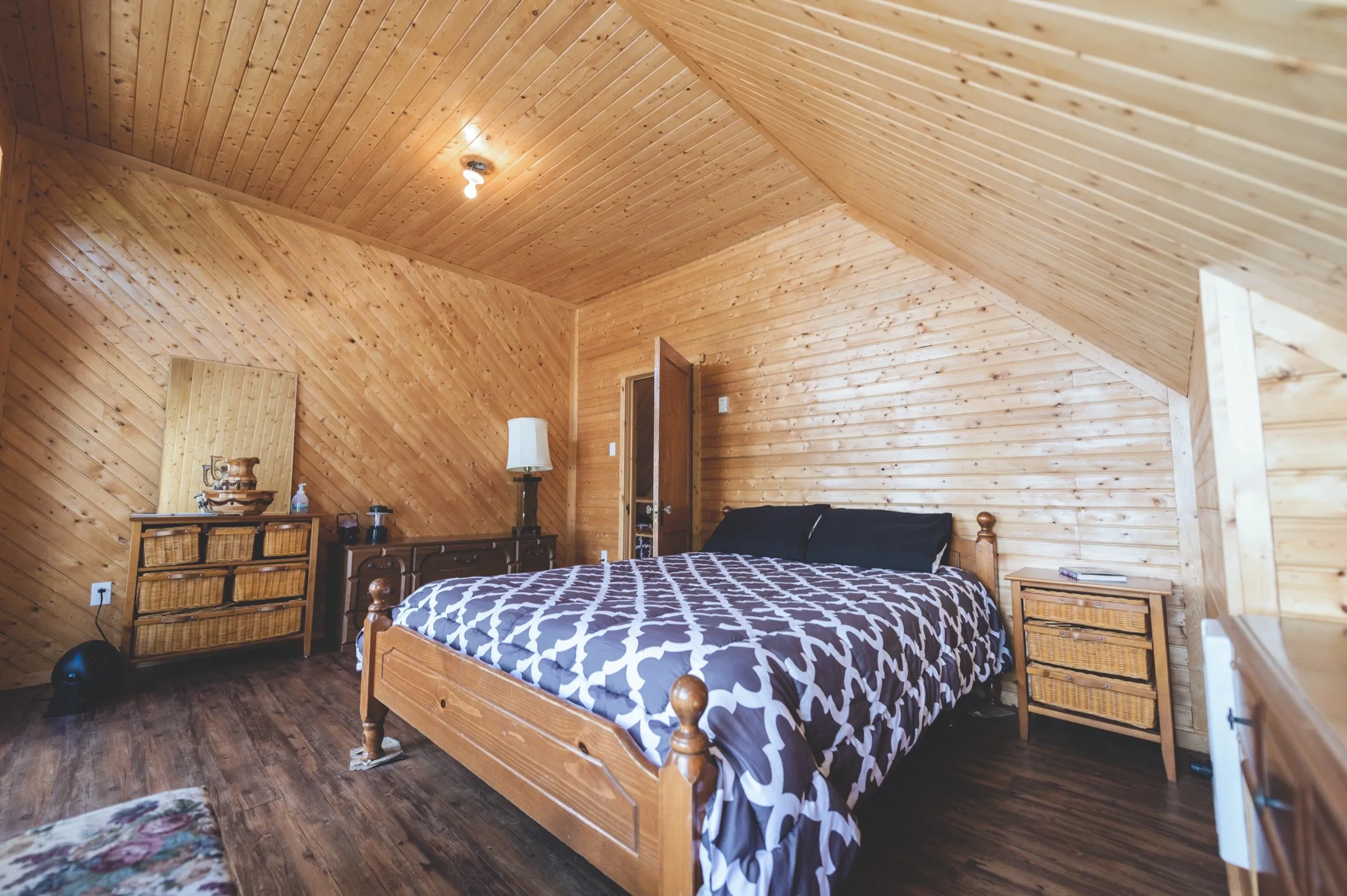 The chalet loft bedroom under a vaulted pine ceiling, with wicker dressers beside the bed