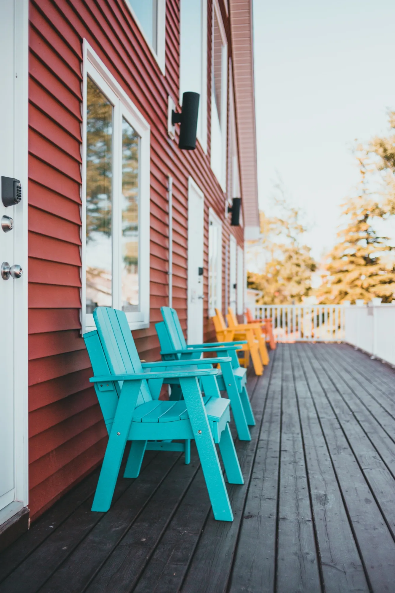 Turquoise and yellow Adirondack chairs set along the upper deck against the red siding