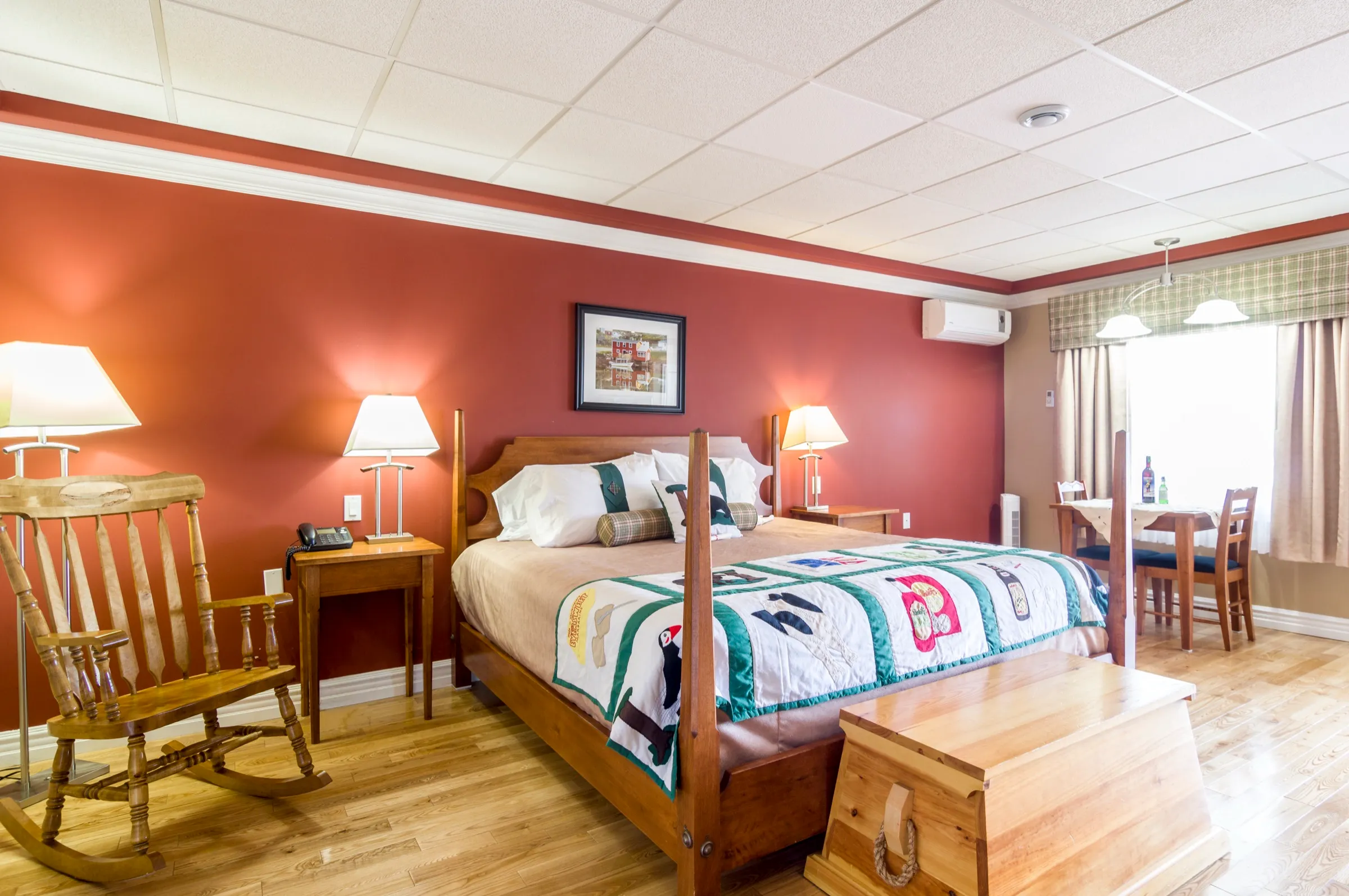 King bed with a carved wooden frame and a Newfoundland appliqué quilt against a terracotta wall