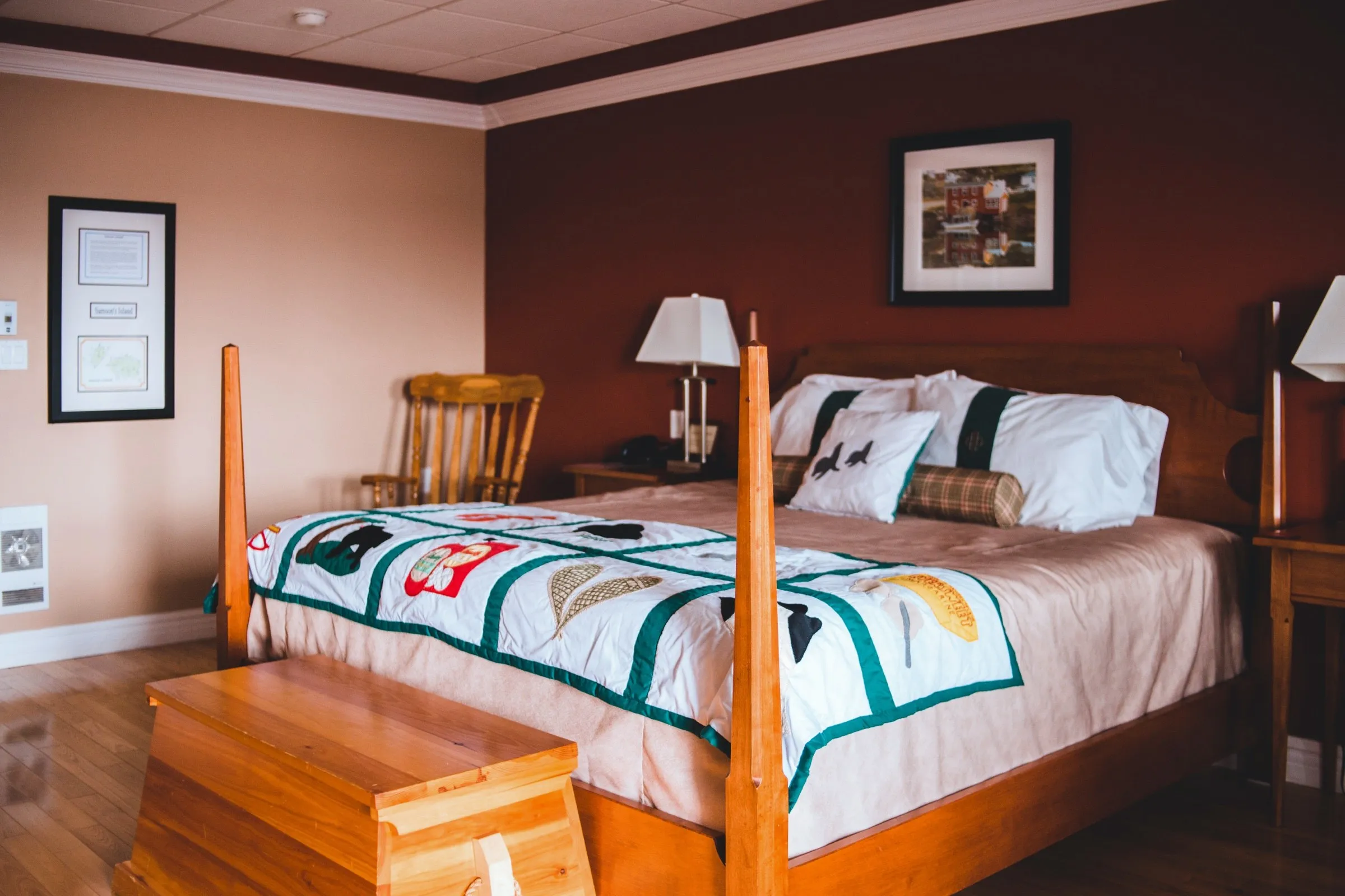Wide view of the King Suite with its king bed, a pine blanket chest at the foot and a framed island map on the wall