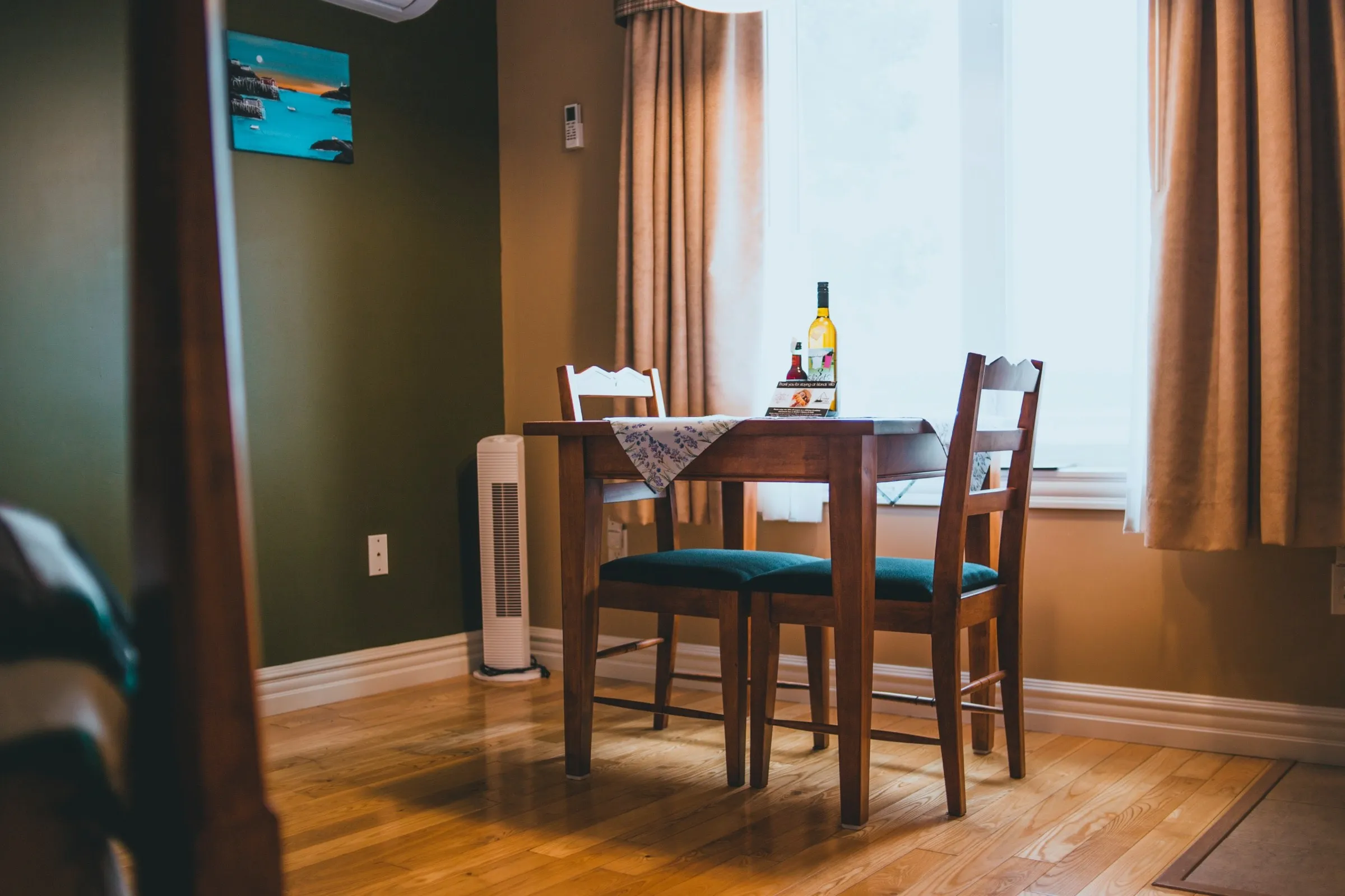 A wooden table and two chairs set in the corner of a suite beneath a window, with bottles of local Newfoundland wine on the table