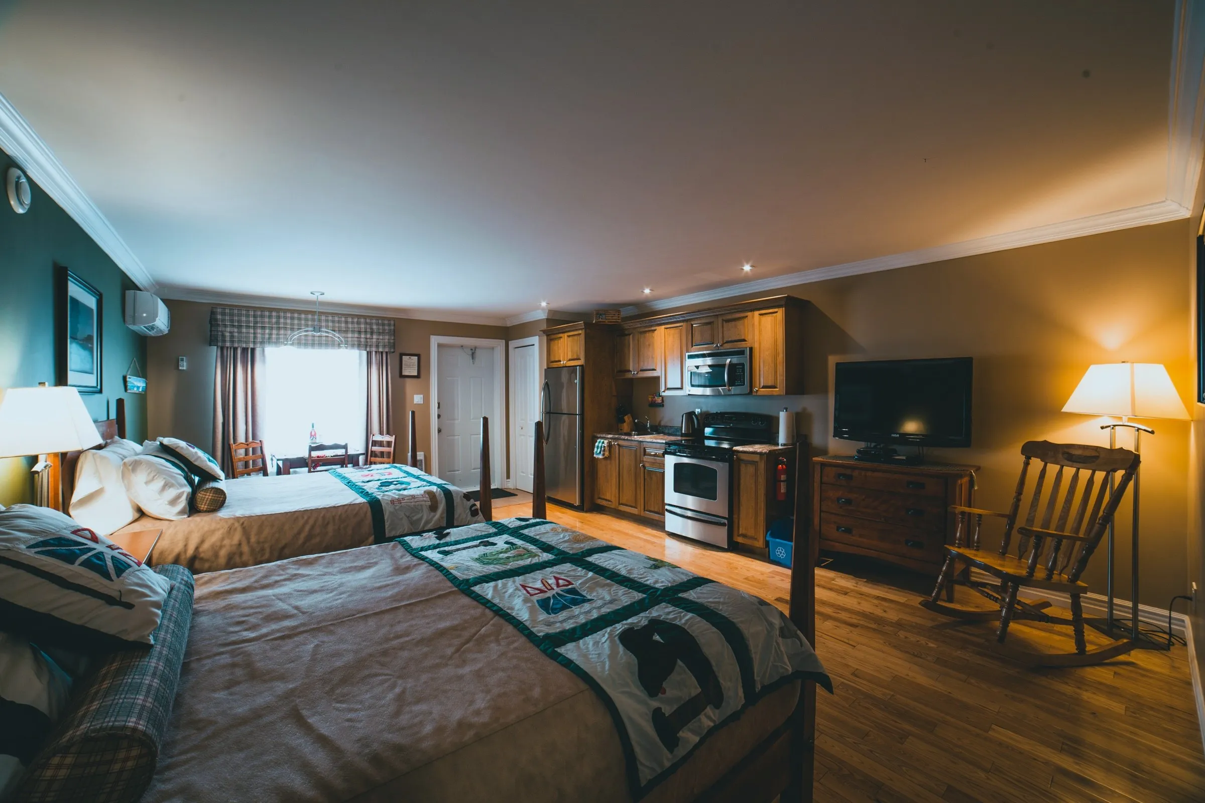 Wide view of the Family Suite showing both queen beds, a rocking chair and the full efficiency kitchen along the far wall
