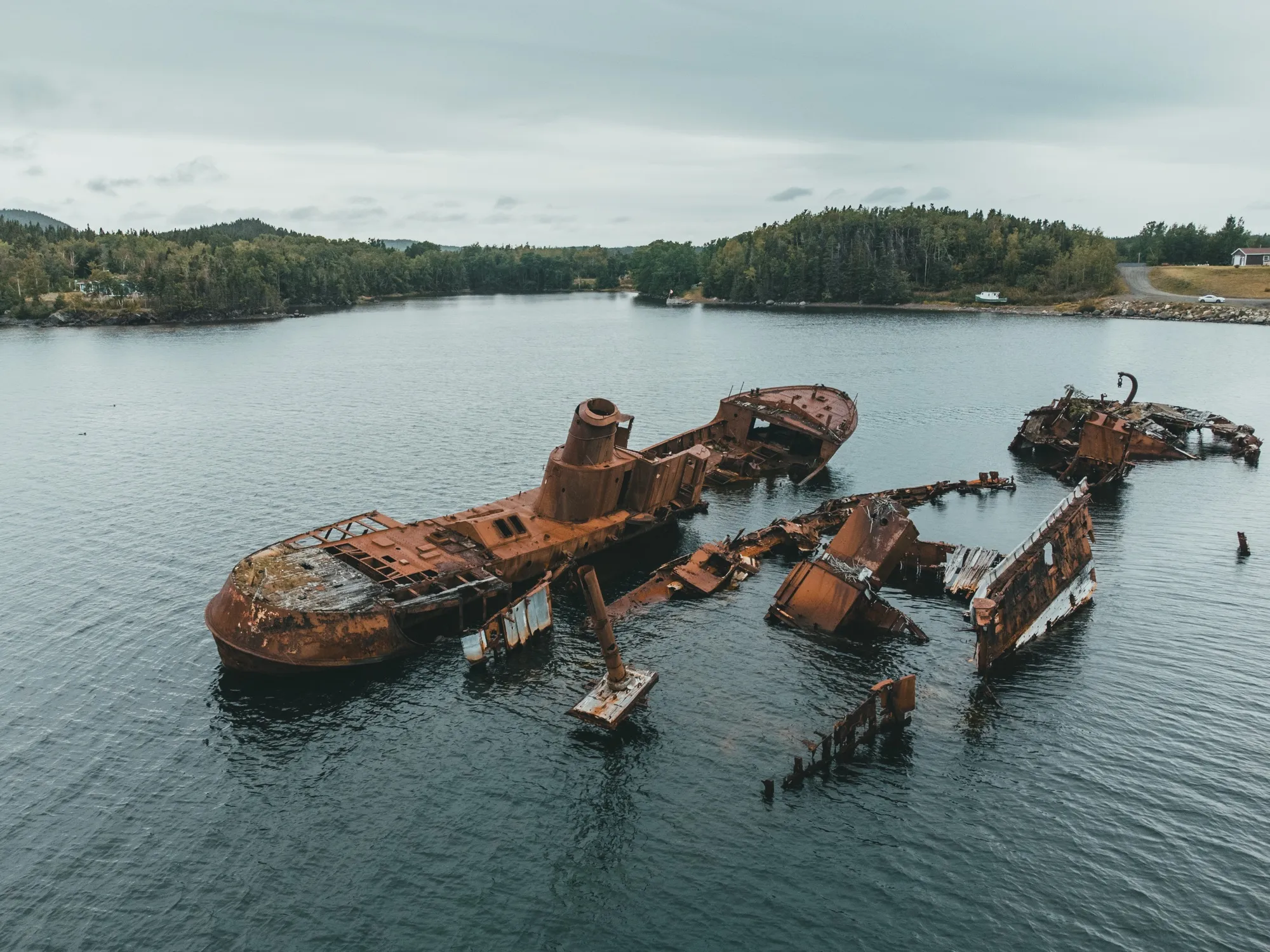 Rusted shipwreck hulls resting in a shallow cove, seen from above