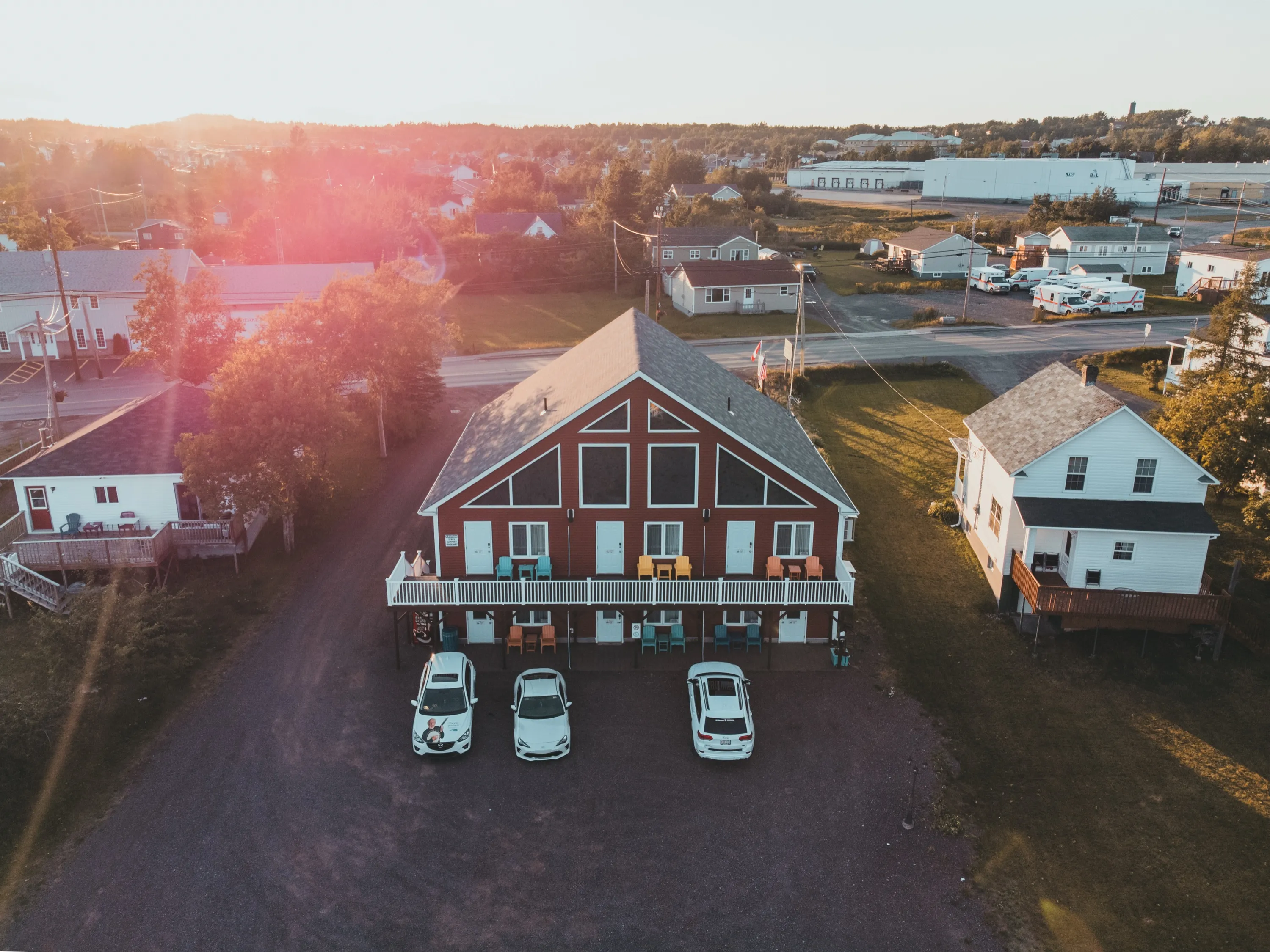 Islands' Villa from above at sunset, colourful Adirondack chairs on both decks and cars in the gravel lot