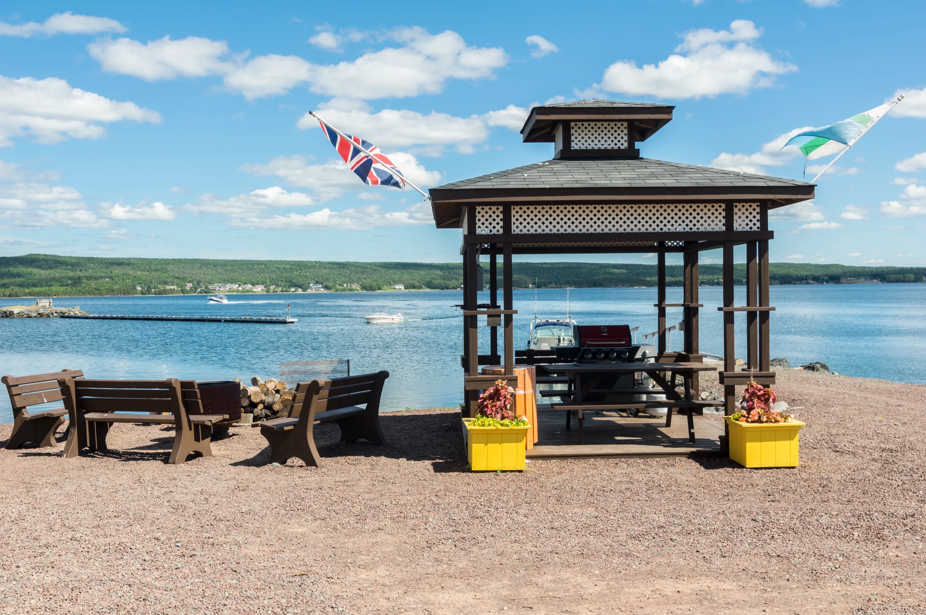 The waterfront BBQ gazebo with picnic tables and flags flying, the blue water of the bay and distant hills beyond