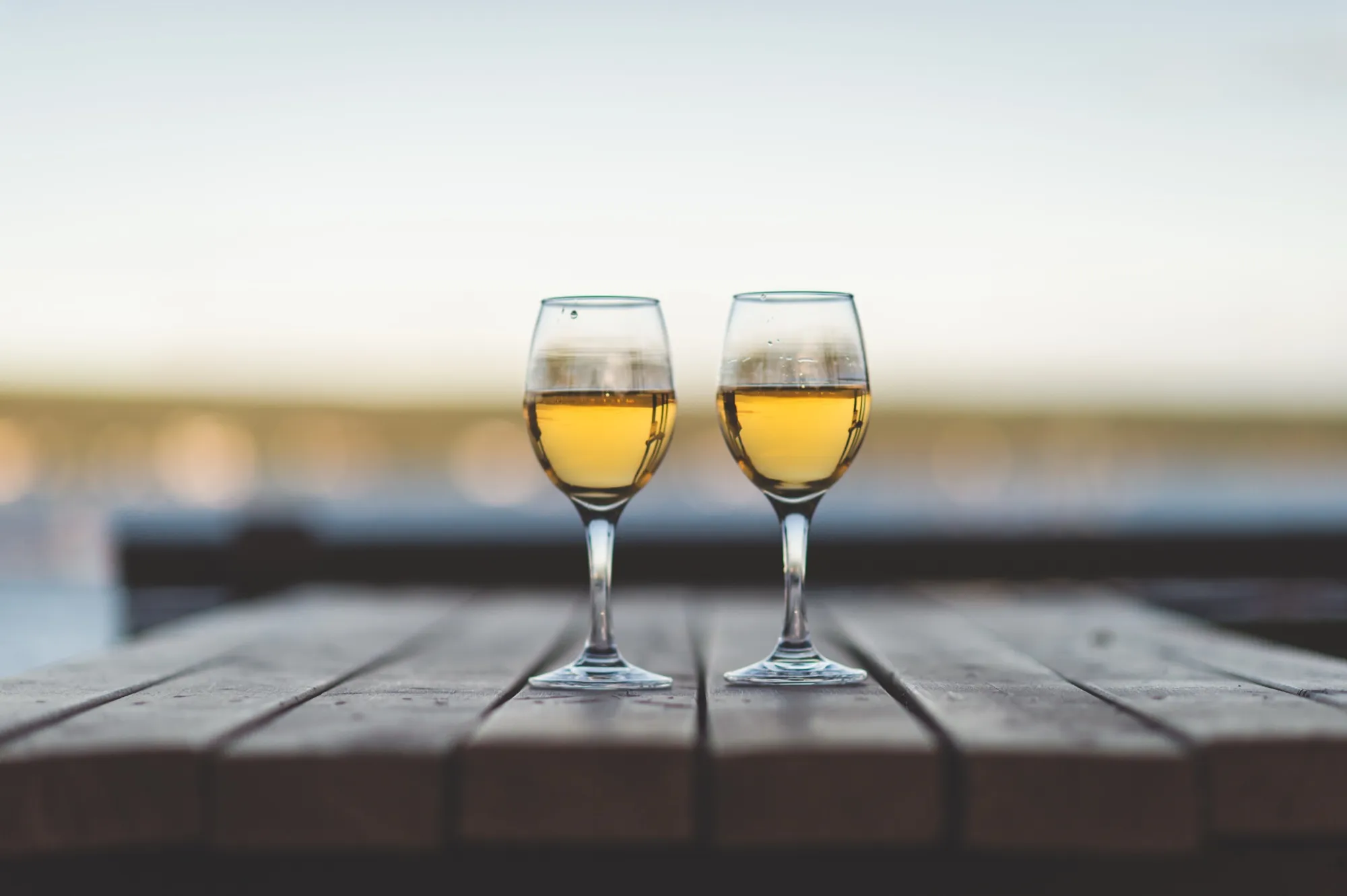 Two glasses of white wine on a weathered picnic table, the harbour soft-focused behind